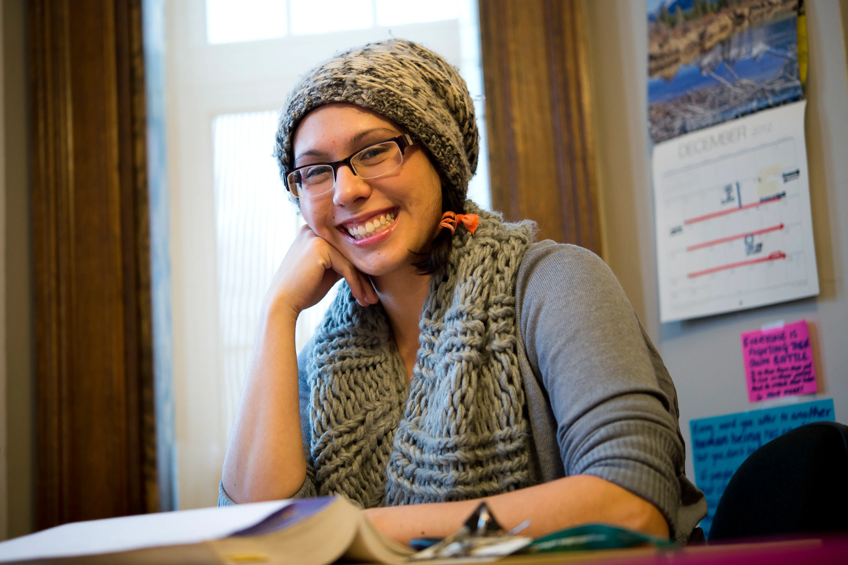 Student with knitted toque and scarf smiling at study desk